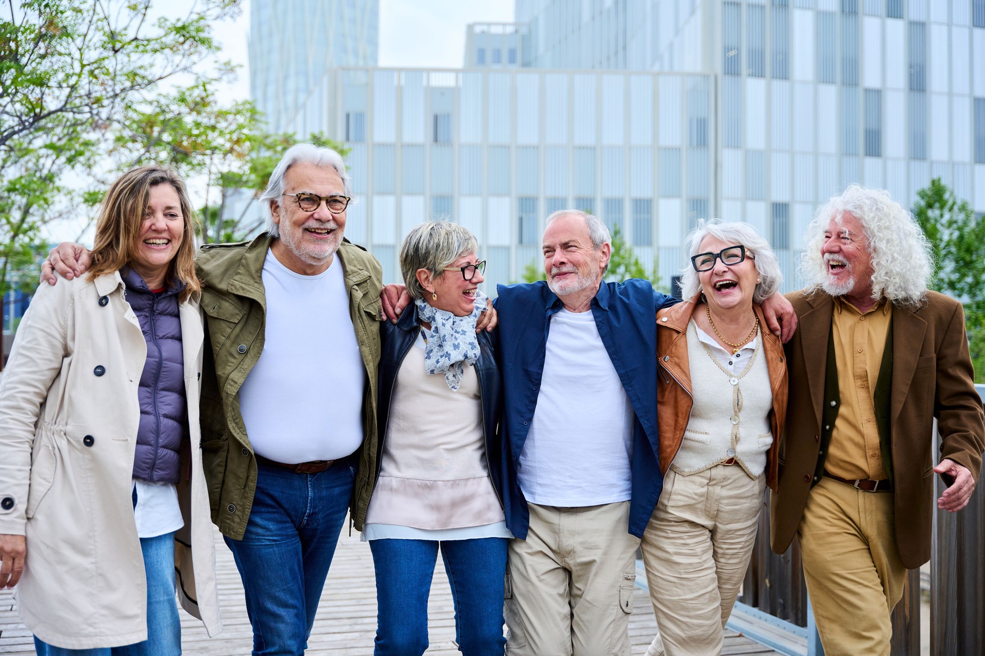 Group of laughing older Caucasian people enjoying holidays strolling hugging in line in urban park.